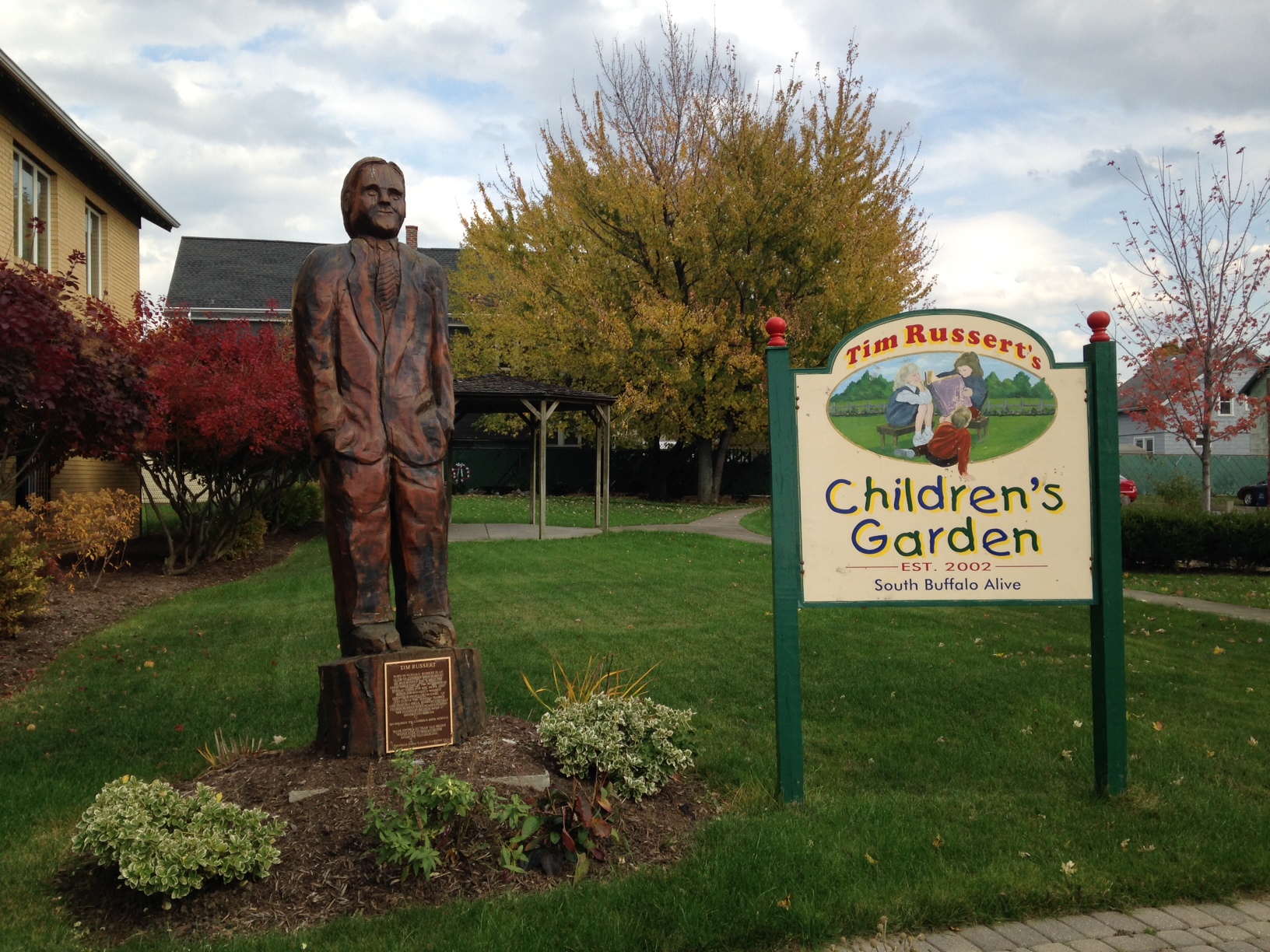 A statue of Tim Ressert stands aside a sign reading "Tim Russert's Children's Garden."