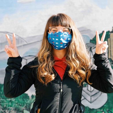 Woman wearing a mask in front of a mural